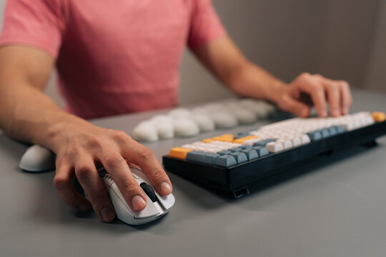 Cropped shot of male hands using mechanical keyboard and mouse, emphasizing comfort and wellbeing with ergonomic cloud-shaped wrist pads on grey desk, focusing on health and innovation in office work.