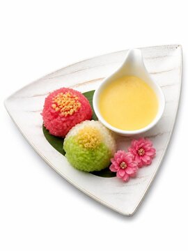Thai sweet sticky rice reimagined into colorful, bite-sized spheres of vibrant pink, green, and white. Topped with crispy mung beans, paired with a rich, egg custard sauce in a teardrop ceramic bowl.