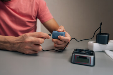 Fototapeta premium Filmmaker plugging lithium-ion battery into multi-slot charging station connected to power strip, ensuring essential camera accessories ready for work, close-up, cropped shot.