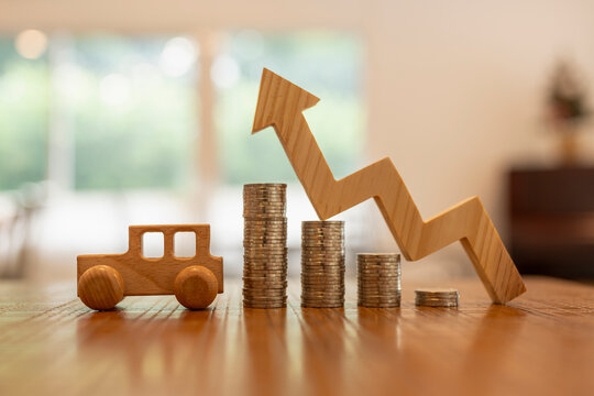 Auto loan and car finance concept with wooden automobile model beside increasing coin stacks and upward trend arrow on reflective table for vehicle insurance savings and automotive investment.