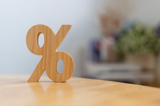Interest rate and discount percentage concept with wooden percent symbol on table against bright soft bokeh background for financial loan calculation, tax promotion and banking investment.