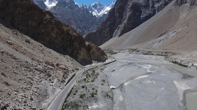 Aerial view of a winding road and dry riverbed through a vast mountain valley under a clear blue sky.
