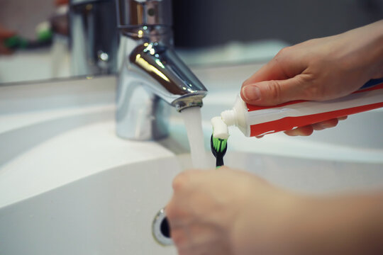 Hands with tooth brush and paste on blurred background in the bathroom in the sink. Selective focus.