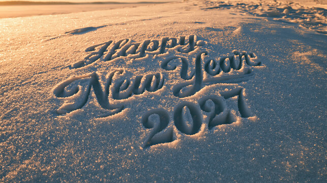 Happy New Year 2027 text written on winter snow surface at sunset.