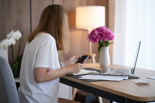 Woman using smartphone while managing bills and home budget