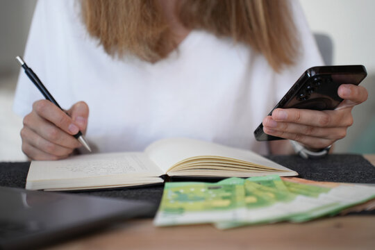 Woman planning household budget with smartphone, notebook and cash