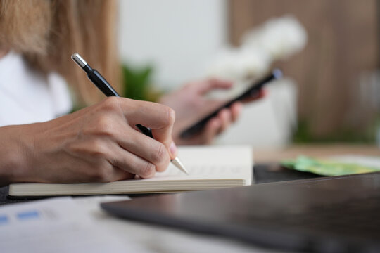 Woman writes notes in a notebook while checking her smartphone at home
