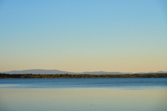 Calm lake with distant hills under clear evening sky