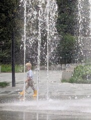 Three-year-old in yellow rain boots chasing the fountain's spray as it drifts in the breeze. Little steps, big smiles.   © gloria