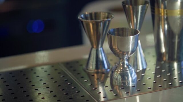 Bartender hand picking up gold jigger from stainless steel professional equipment set on modern counter.