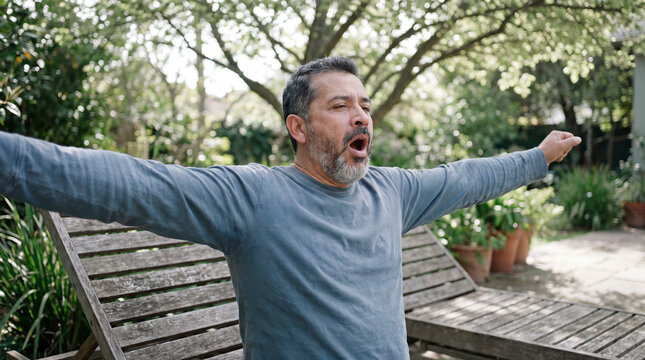 Invigorated senior man stretches arms wide breathing deeply in home garden