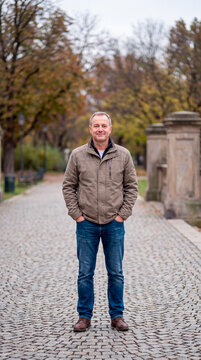 Composed mature man stands confidently on tree-lined path in autumn park