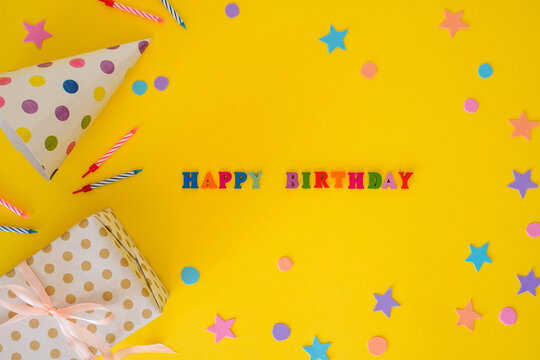 Birthday card with a party hat, festive candles, and a gift on a yellow background with a text Happy Birthday