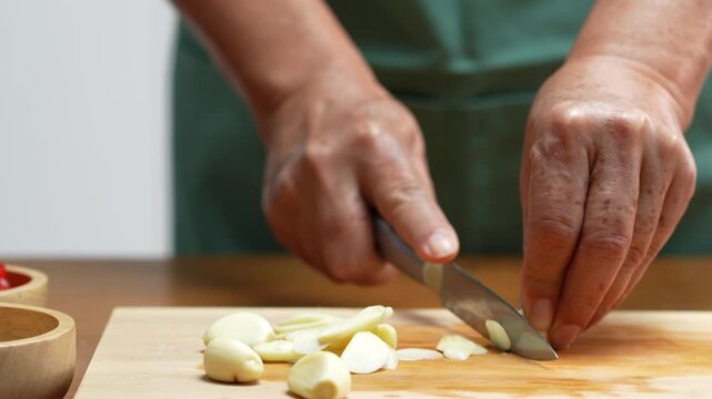 Hands chopping fresh garlic with a kitchen knife for homemade cooking.