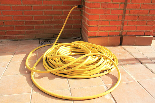 Manguera amarilla de jardiner&iacute;a, limpieza, riego y mantenimiento enredada y liada en suelo de patio y ladrillo 