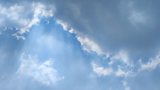 Dramatic heavenly sun rays breaking through dark clouds into blue sky