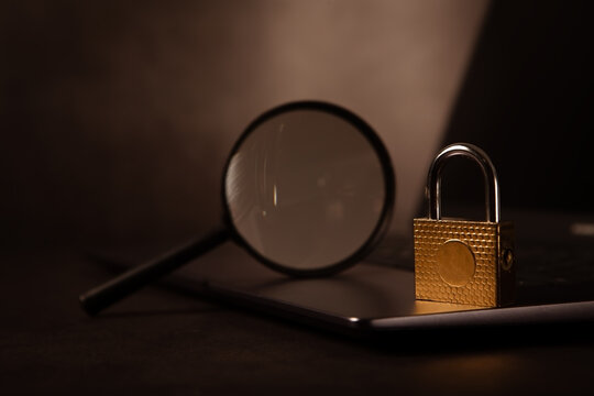 laptop, magnifying glass and a padlock on a dark background