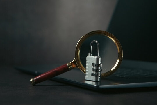 laptop, magnifying glass and a padlock on a dark background