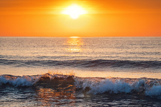 Bright sun rising over sea with crashing crest waves illuminated by golden sunlight