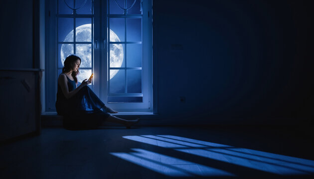 Woman browsing smartphone by window with full moon glow at night