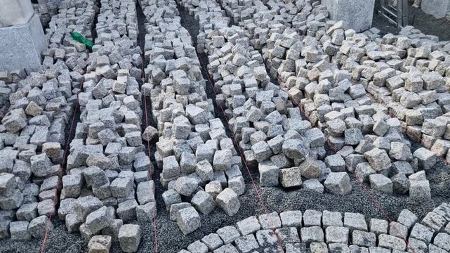 staging technique used by masons during large-scale cobblestone paving setting fan patterns or arcs ​Material Distribution: Loose cobblestones sett pavers are pre-distributed into organized parallel r