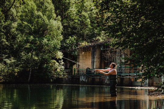 Young man casting fishing rod while fly fishing in a forest river