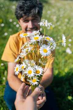 Man gives a daisy bouquet to a woman in a summer field