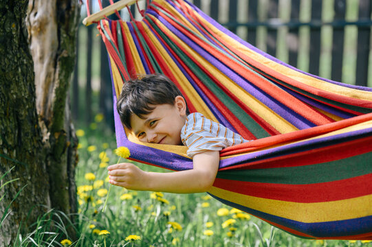 Smiling in a colorful hammock holding a yellow dandelion outdoors