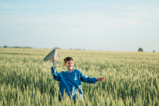 Smiling boy launches a paper airplane in a green field