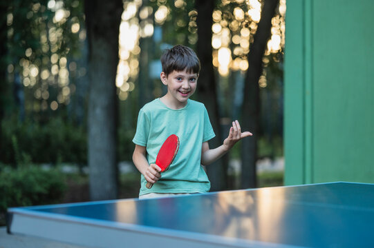 Smiling boy plays table tennis outdoors