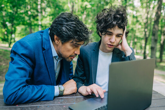 Man and teenage boy solve a problem on a laptop outdoors