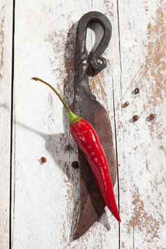 Red chili pepper (Capsicum) and an old knife on white wooden table, studio shot