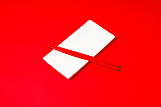 Red chopsticks lie on a white sushi plate over a red background
