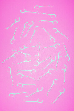 Many dental floss picks lie scattered on a pink background