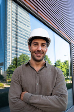 Smiling male architect wearing a hardhat stands outside a building
