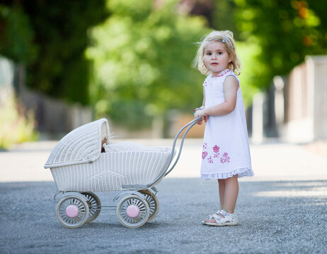 Germany, Bavaria, Girl (2-3) playing with toy baby carriage