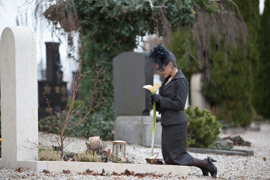 Germany, Bavaria, Young woman visiting a tombstone in cemetery