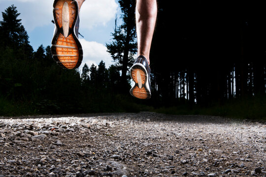 Low angle view of a man jogging on a gravel path in a forest