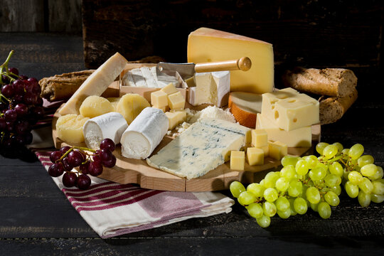 Cheese platter with different sorts of cheese, baguette and grapes on wood