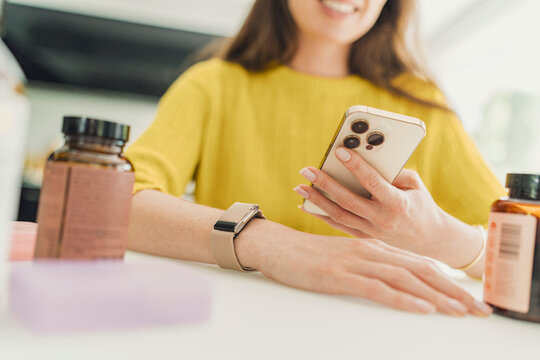 Smiling woman holds smartphone near fitness tracker and supplement