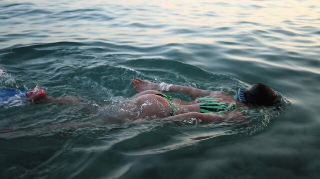 Woman snorkeling in mask and fins swims through clear sea at sunset kicking through gentle waves while enjoying underwater exploration and active summer recreation at sea
