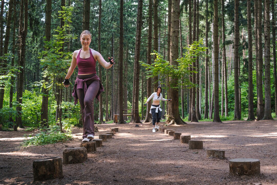 Friends balance on wooden stumps during an outdoor forest workout