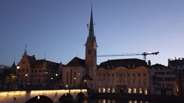 View of the historic Fraumunster church illuminated at dusk with a bridge in the foreground and a construction crane in the background in Zurich, Zurich, Switzerland.