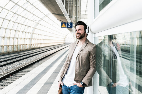 Smiling young man wearing headphones waiting at the station platform