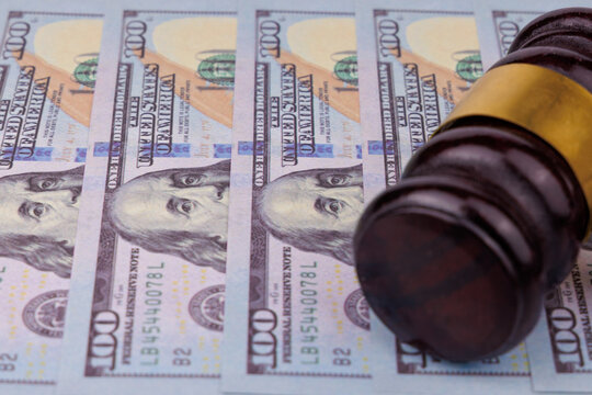 High angle perspective of a dark mahogany judge gavel lying above neatly organized hundred Dollar cash bills on a gray concrete desk, lawsuit damages, bail payment, and legal penalty visual