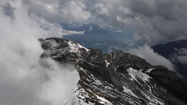 View of Mount Pilatus peak emerging from thick clouds with rocky terrain and snow patches in Alpnach, Obwalden, Switzerland.