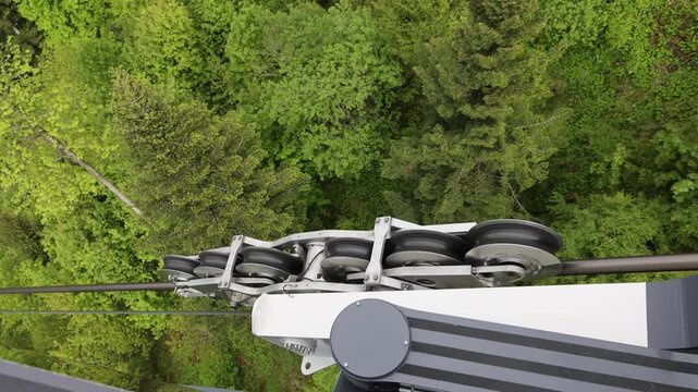View of the Stanserhorn-Bahn cable car pulley system moving along the cable above dense green forest in Stans, Nidwalden, Switzerland.