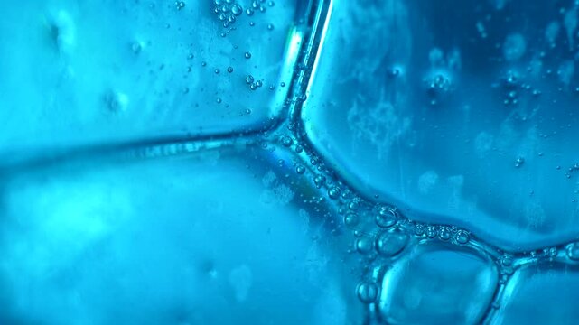 Abstract macro shot of green liquid with slow-moving bubbles and changing colors in ultraviolet light.