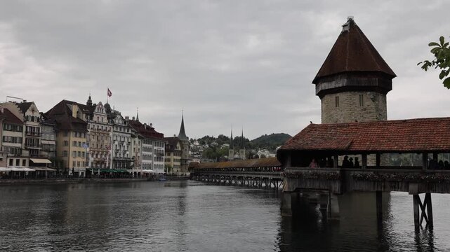 View of the historic Kapellbrucke wooden bridge spanning the Reuss River with traditional architecture and the Wasserturm tower in the background in Lucerne, Lucerne, Switzerland.