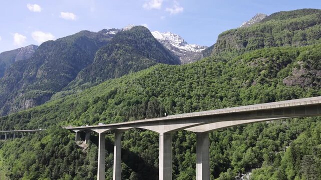 View of the Gotthard Panorama Express SBB railway viaduct spanning a lush green valley with a river below in Lugano, Ticino, Switzerland.